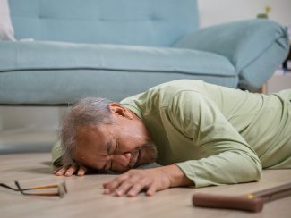Elder man falling on the floor alone with walking stick on living room at home